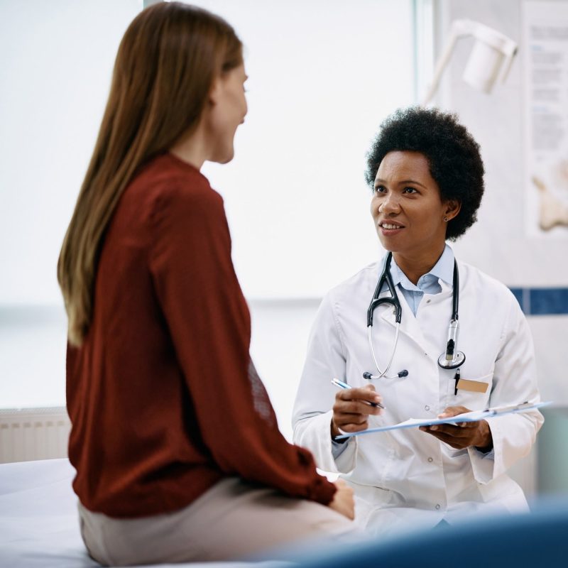 Black female doctor talking to a woman during medical appointment in the hospital.